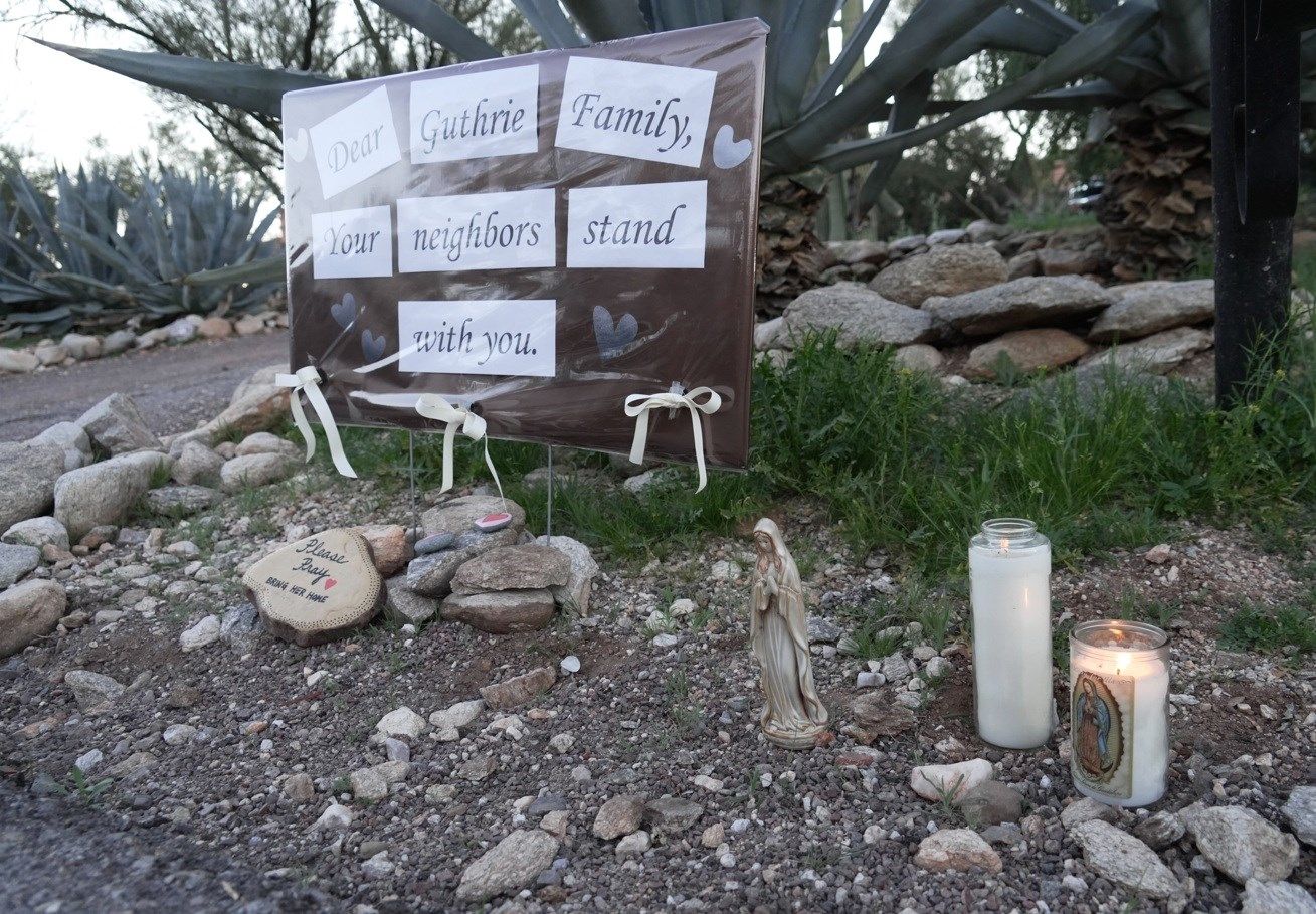 Lit candles next to a sign from neighbors supporting the Guthrie family outside of Nancy Guthrie’s house